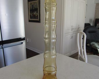 May include: A tall, amber glass vase with a textured, ribbed design. The vase has a wide base and a narrow neck.