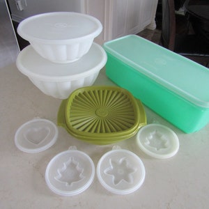 May include: A set of vintage green, white and olive green plastic storage containers. The set includes a rectangular container with a lid, a round bowl with a lid, and five smaller round containers with lids. Each of the smaller containers has a different shape cut out of the lid.