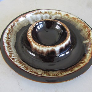 May include: A brown and white glazed ceramic chip and dip serving dish with a raised centre bowl. The dish has a brown rim and a white and brown glaze pattern.