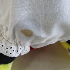 May include: Close-up of a white fabric with a brown stain. The fabric has a ruffled edge with a decorative eyelet trim. The bottom of the image shows a yellow and black object.