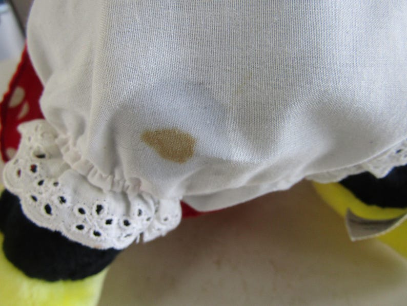 May include: Close-up of a white fabric with a brown stain. The fabric has a ruffled edge with a decorative eyelet trim. The bottom of the image shows a yellow and black object.