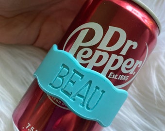 May include: A blue can koozie with the name "BEAU" printed on it. The koozie is on a red can of Dr Pepper, which says "Est. 1885" on it. The can is 7.5 fl oz (221 ml).