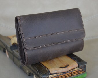 May include: A brown leather wallet with a stitched seam across the front. The wallet is sitting on a wooden toy car.