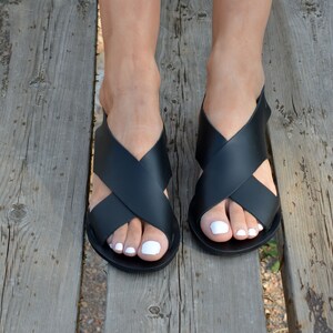 May include: Black leather sandals with a criss-cross strap design. The sandals have a flat sole and are worn on a person's feet.