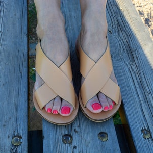 May include: A pair of tan leather sandals with criss-cross straps and red nail polish on the toes.
