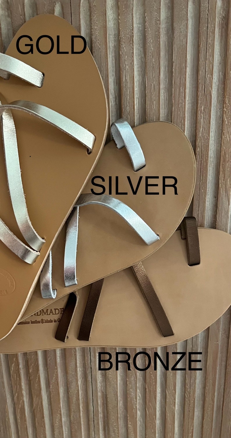 Puede incluir: Primer plano de tres pares de sandalias de cuero en dorado, plateado y bronce. Cada sandalia tiene una suela marr&oacute;n claro y correas finas en el color met&aacute;lico correspondiente. Las sandalias est&aacute;n hechas a mano.