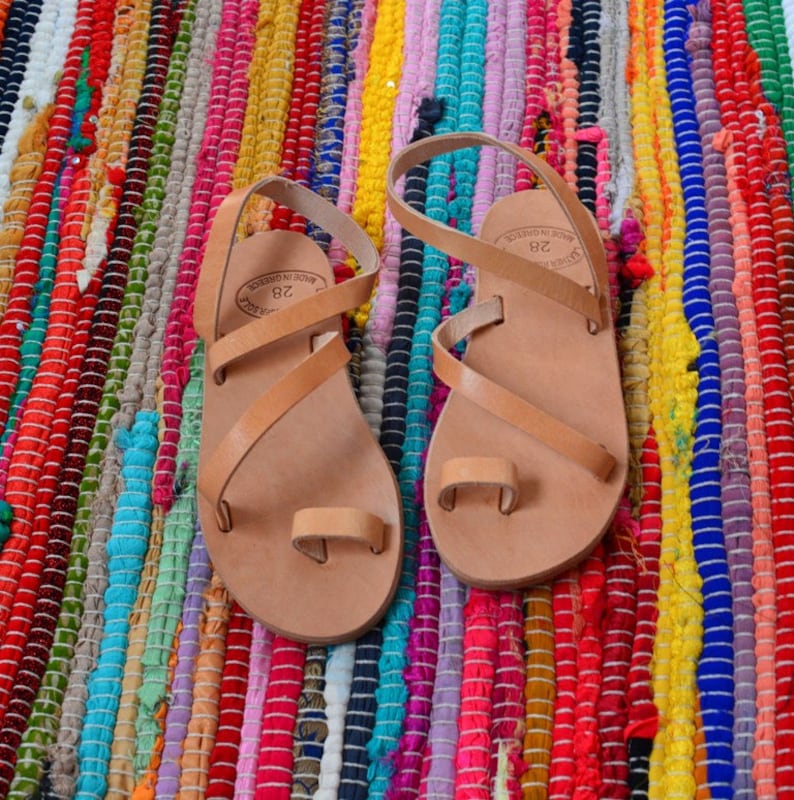 Pu&ograve; includere: Un paio di sandali in pelle color cuoio con un passante per l'alluce e pi&ugrave; cinturini. I sandali sono realizzati in Grecia e hanno la taglia 38 stampata sui cinturini.