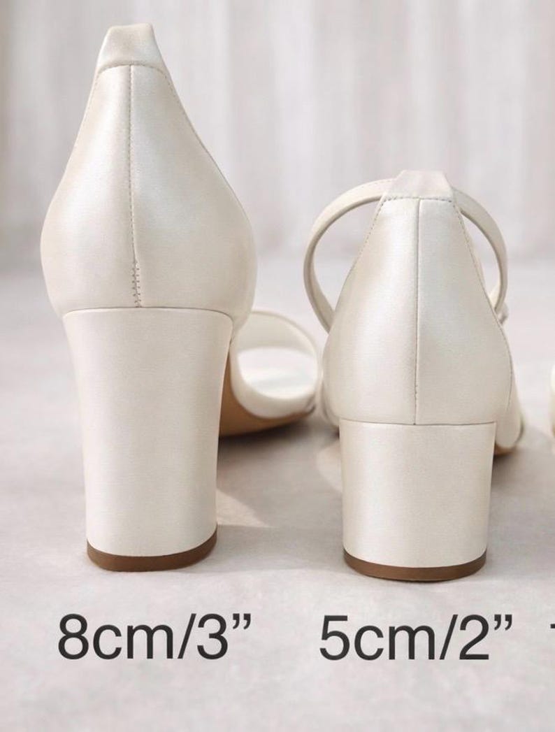 Op de afbeelding: Twee paar ivoorkleurige sandalen met blokhak. E&eacute;n paar heeft een hak van 8 cm (3"), de andere een hak van 5 cm (2"). De sandalen hebben een eenvoudig ontwerp met een enkelbandje.
