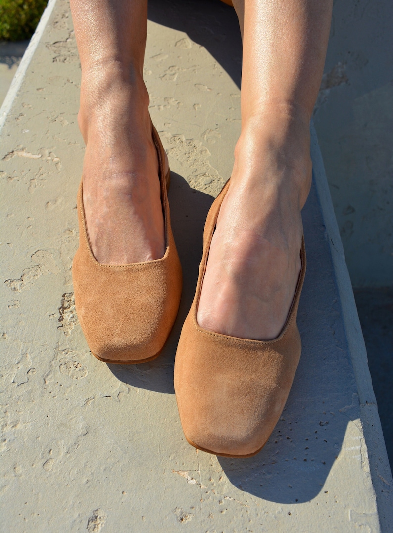 May include: A pair of light brown suede ballet flats with a square toe.