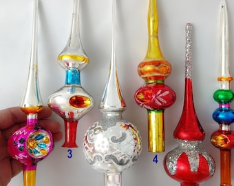Puede incluir: Una colección de siete puntas de árbol de Navidad de vidrio vintage en varias formas y colores, incluyendo plata, rojo, oro, azul y rosa. Cada punta presenta una aguja larga y puntiaguda y una base hueca, numeradas del 1 al 7.