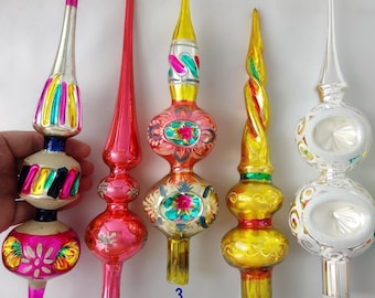 Puede incluir: Seis puntas de árbol de Navidad de vidrio vintage dispuestas en fila. Cada adorno presenta una forma de aguja alargada única con detalles pintados coloridos, incluyendo acabados metálicos en plata, oro, rojo, rosa, amarillo y turquesa con motivos florales.