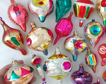 May include: A collection of twenty-two vintage glass Christmas ornaments in various shapes and colors, including pink, red, gold, green, and purple. Each ornament is numbered from 1 to 22 and features metallic finishes, reflective surfaces, and painted details.