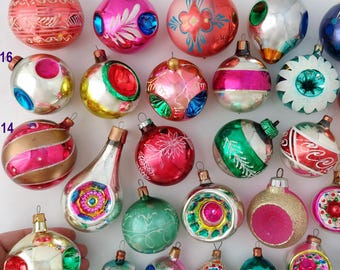 May include: A collection of vintage glass Christmas ornaments in various shapes and colors, including spheres, teardrops, and indented designs. The ornaments feature metallic finishes, painted floral patterns, and glitter accents, each labeled with a small purple number.