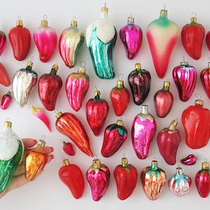 Puede incluir: Una colección de adornos navideños de vidrio vintage con forma de pimientos y fresas. Los adornos son de varios colores, incluyendo rojo, verde, rosa y blanco.