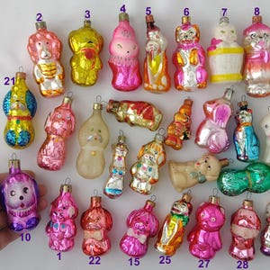 May include: A selection of antique Christmas tree decorations, mainly animal-shaped. The glass ornaments feature dogs, cats, and bears in shades of pink, gold, and blue. Some have painted details and metallic finishes. A nostalgic festive collection.