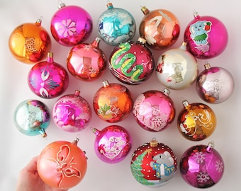 May include: A collection of vintage Christmas ornaments in various colors and designs. The ornaments feature a variety of patterns, including snowflakes, flowers, and animals. Some of the ornaments are shiny, while others are matte.