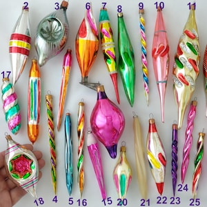 May include: A collection of twenty-five vintage glass Christmas ornaments in various elongated, twisted, and teardrop shapes. The ornaments feature metallic, glossy, and translucent finishes in colors including red, green, gold, pink, blue, and orange.