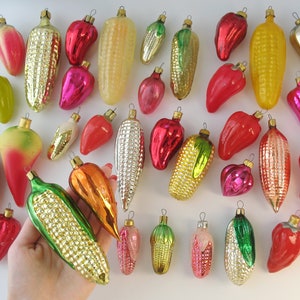 Puede incluir: Una colección de adornos navideños de vidrio vintage con forma de mazorcas de maíz y pimientos. Los adornos son de varios colores, incluyendo rojo, verde, amarillo y dorado.