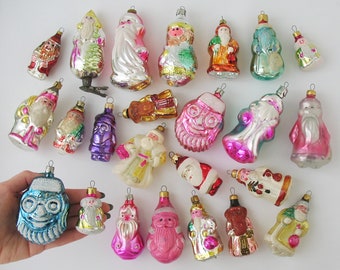 May include: A collection of vintage glass Christmas ornaments featuring Santa Claus in various poses and colors. The ornaments are hand-painted and have a traditional look.