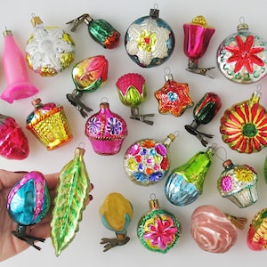 May include: A collection of vintage Christmas ornaments in various shapes and colors. The ornaments include a pink tulip, a yellow pear, a green leaf, and a pink egg. The ornaments are made of glass and have metal clips.