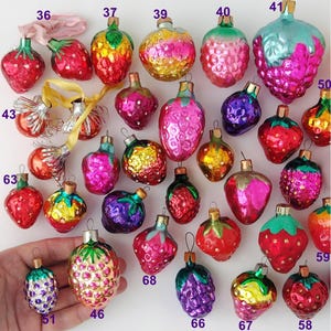 May include: A collection of 20 vintage glass Christmas ornaments shaped like strawberries. The ornaments are in various colors, including red, pink, green, yellow, and blue. Some of the ornaments have a shiny finish, while others have a matte finish.