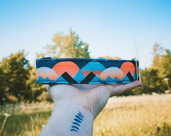 Puede incluir: Un collar de perro colorido con un patrón geométrico de montaña y puesta de sol. El collar es azul, naranja y negro.