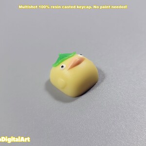 May include: A yellow resin keycap shaped like a cartoon chick wearing a green leaf hat. Multishot 100% resin casted keycap. No paint needed!