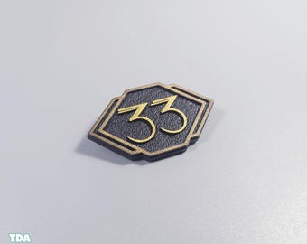 May include: A black and gold art deco style plaque with the number "33" in gold. The plaque has a geometric shape with a black background and gold trim. The number "33" is in a stylized font.