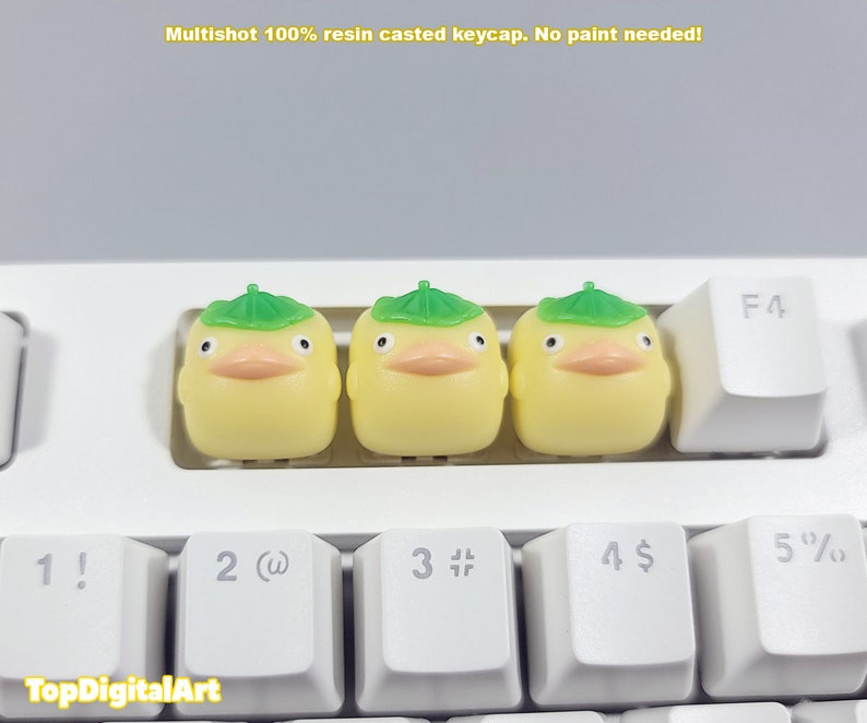 May include: Three yellow duck keycaps with green leaf hats. The keycaps are on a white keyboard with black keys.