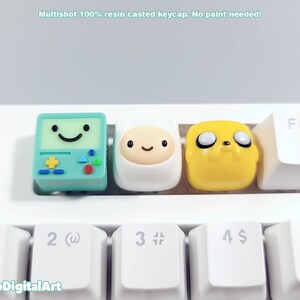 May include: Three resin keycaps featuring characters from the animated series Adventure Time. The keycaps are green, white, and yellow and feature Finn the Human, Jake the Dog, and BMO.