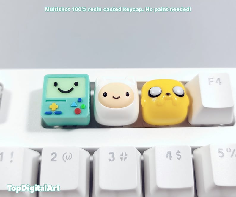 May include: Three resin keycaps featuring characters from the animated series Adventure Time. The keycaps are green, white, and yellow and feature Finn the Human, Jake the Dog, and BMO.