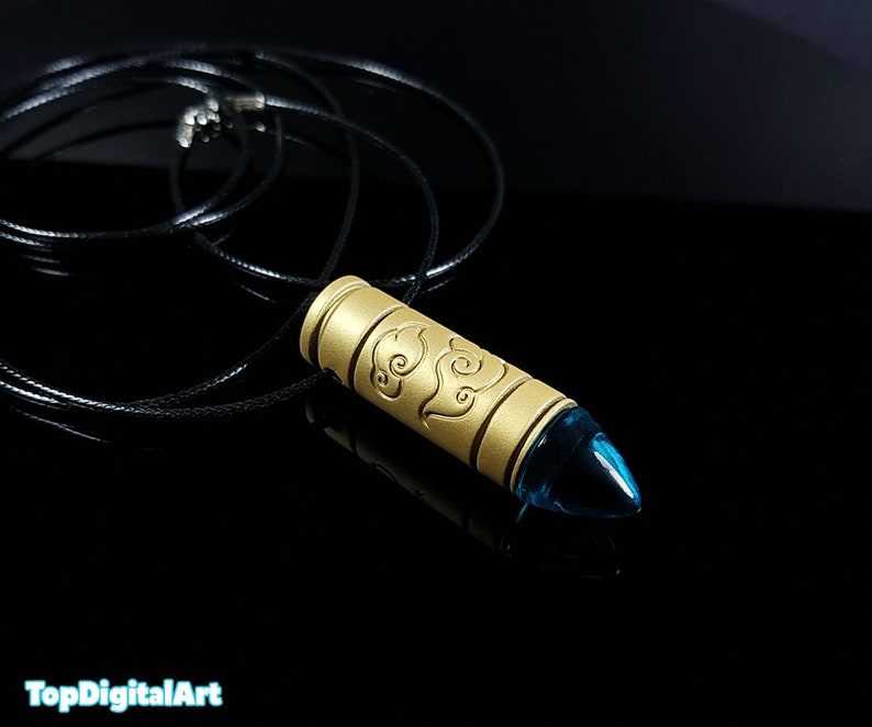 May include: Gold bullet pendant necklace with a blue gem at the tip and a design of clouds on the side. The necklace is on a black cord.