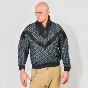 Puede incluir: Un suéter de patrón gris y negro con ribete de cuero negro y cuello en V.