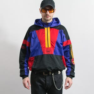Puede incluir: Chaqueta anorak Adidas vintage en negro, azul, rojo y amarillo. La chaqueta presenta un diseño de bloques de color con capucha, cierre de media cremallera y el logo de Adidas. Las mangas tienen las tres rayas de Adidas.