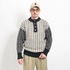 May include: A black and white patterned sweater with a button-up collar and a black trim. The sweater has a geometric pattern and is made of a thick knit fabric.