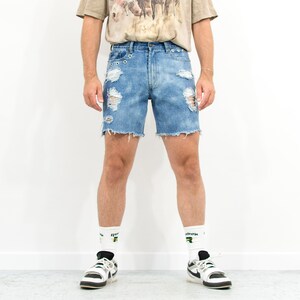 May include: Light blue denim shorts with distressed details and frayed edges. The shorts have multiple rips and tears throughout the fabric.