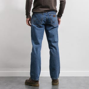 May include: Blue denim jeans with a brown leather patch on the back pocket. The jeans have a classic five-pocket design and a straight leg fit. The person is wearing a brown sweater and brown boots.