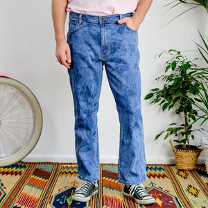 K&ouml;nnte beinhalten: Eine Person tr&auml;gt eine blaue Jeans mit einem verblassten Batik-Muster. Die Jeans hat einen geraden Schnitt und wird mit schwarzen Turnschuhen getragen.