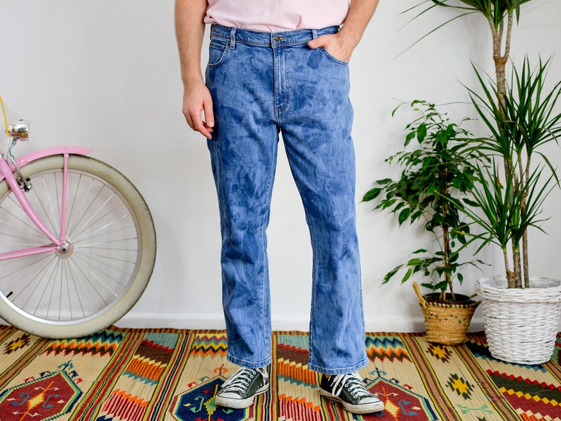 K&ouml;nnte beinhalten: Eine Person tr&auml;gt eine blaue Jeans mit einem verblassten Batik-Muster. Die Jeans hat einen geraden Schnitt und wird mit schwarzen Turnschuhen getragen.