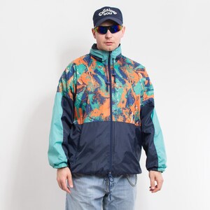 Puede incluir: Una chaqueta con estampado azul, naranja y verde con cierre de cremallera. La chaqueta tiene un cuello alto y un cordón de ajuste en la cintura.