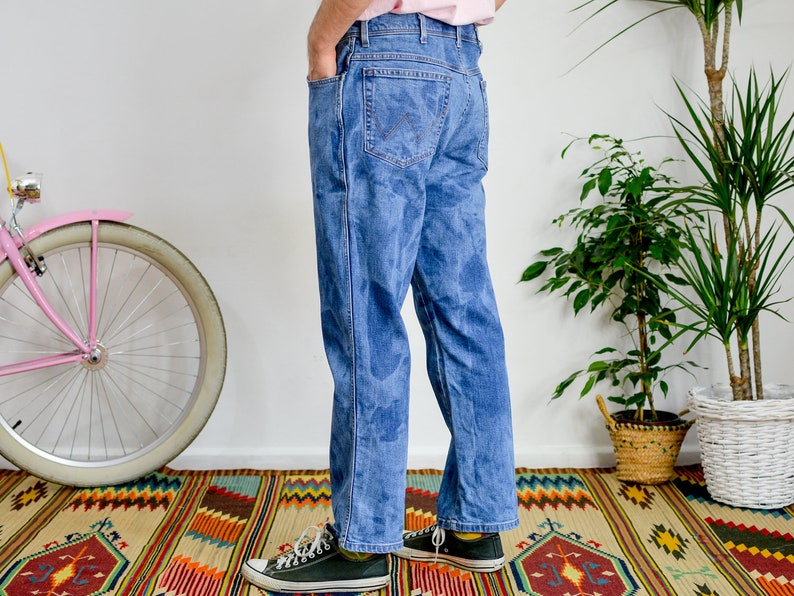 K&ouml;nnte beinhalten: Eine Person tr&auml;gt eine blaue Jeans mit einem verblassten Batik-Muster. Die Jeans ist locker geschnitten und hat ein gerades Bein. Die Person tr&auml;gt schwarze Turnschuhe.