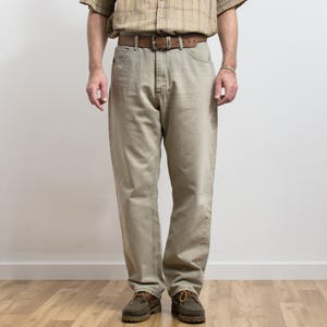 Könnte beinhalten: Khakifarbene Hose mit einem braunen Ledergürtel und einem Hemd mit Knöpfen. Die Hose hat eine lockere Passform und wird mit braunen Schuhen kombiniert. Das Outfit ist lässig und für den Alltag geeignet.