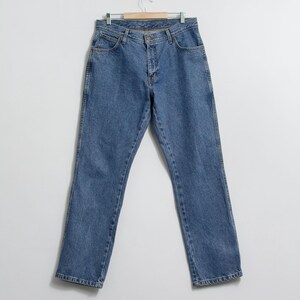 May include: A pair of light blue denim jeans hangs from a wooden hanger. The jeans have a classic five-pocket design, a button and zipper closure, and a straight leg cut. The denim has a medium wash with subtle fading.