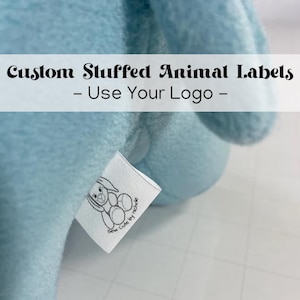 Puede incluir: Un peluche azul claro con una etiqueta blanca adjunta. La etiqueta presenta una ilustración en blanco y negro de un conejito y el texto "Sew Cute by nicole". El texto "Custom Stuffed Animal Labels - Use Your Logo -" se muestra arriba.