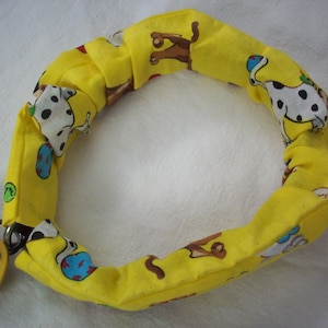 May include: A yellow dog collar with a repeating pattern of cartoon dogs and colorful accents. The collar has a metal ring and a bone-shaped tag that reads "BENJI".