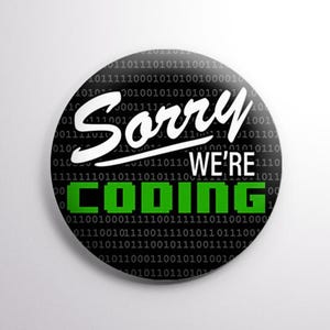 May include: A round black button with the text "Sorry We're Coding" in white and green. The background features a binary code pattern. A fun accessory for programmers and tech enthusiasts.