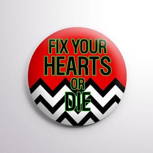 May include: A round button with a red background and the text "FIX YOUR HEARTS OR DIE" in green and black. A black and white zig-zag pattern borders the bottom of the button.