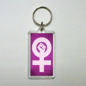 May include: A purple keychain with a white feminist symbol featuring a fist inside a circle.