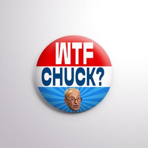 May include: A round button with a red and white top, blue and white stripes in the middle, and a blue burst design at the bottom. The button has the text "WTF CHUCK?" and a photo of a man wearing glasses.