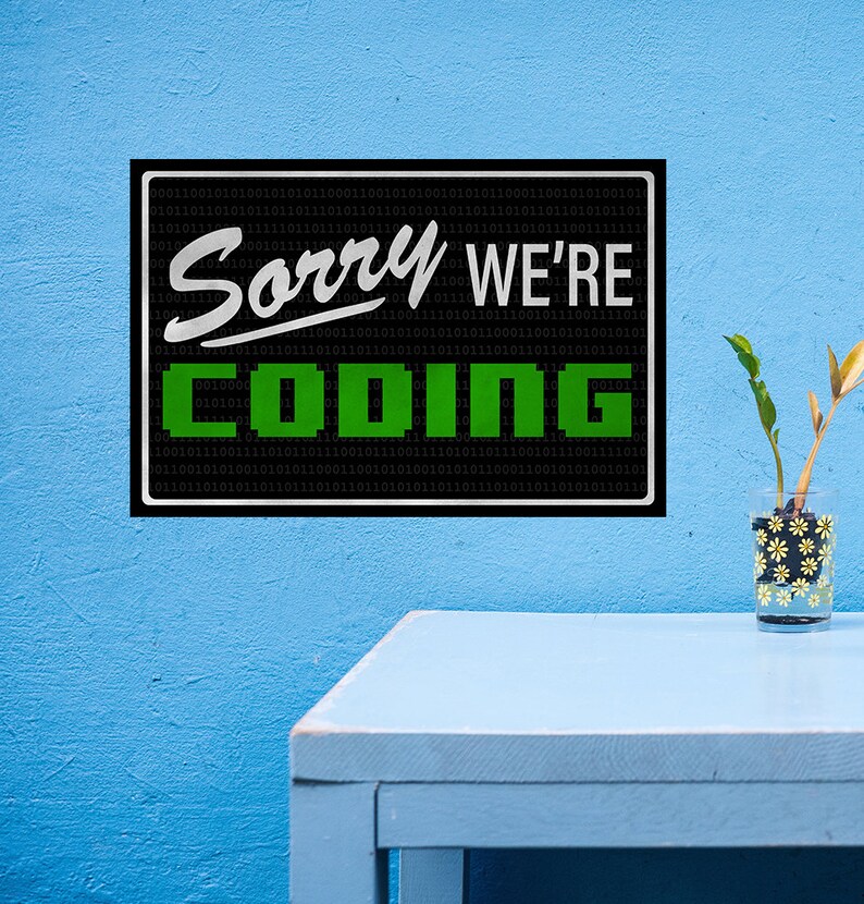 May include: Black and white sign with green text that reads "Sorry We're Coding" on a blue wall. The sign is surrounded by a pattern of 0s and 1s.